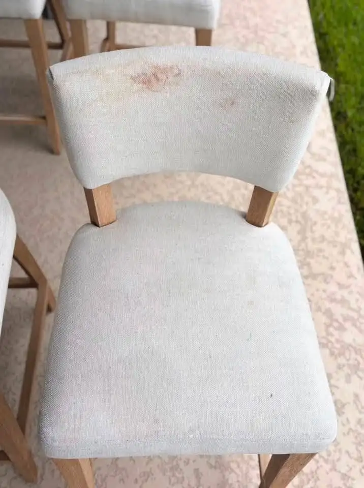 Cream linen dining chair with an orange-brown stain on the curved backrest