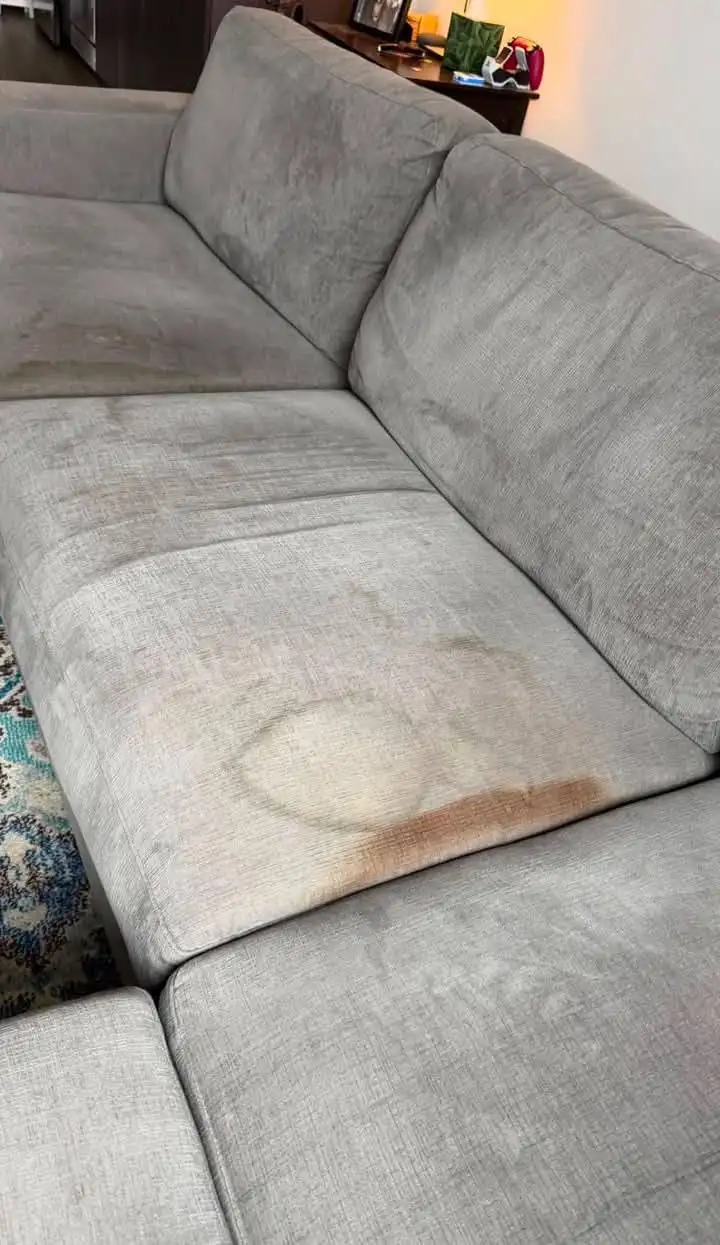 Grey fabric sofa with heavy body soiling and a large brown ring stain on the seat