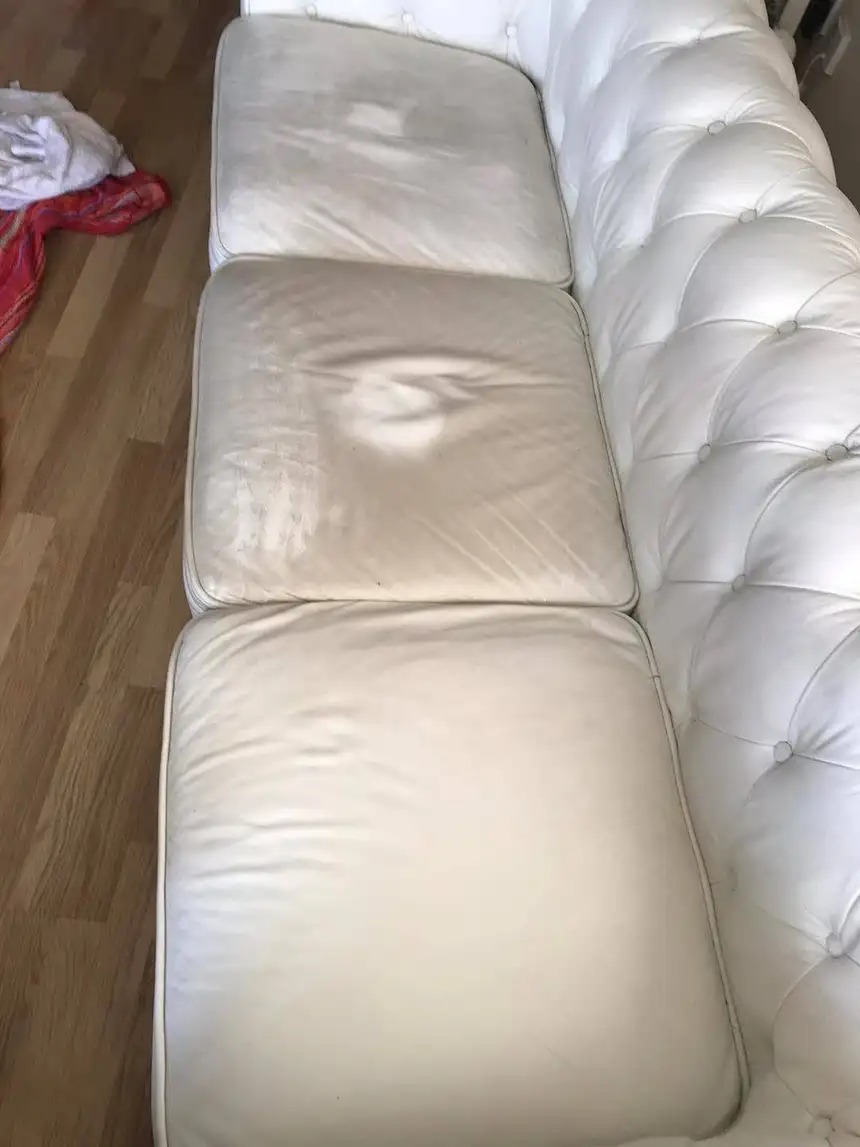 White leather chesterfield sofa with yellowed, grey-streaked seat cushions