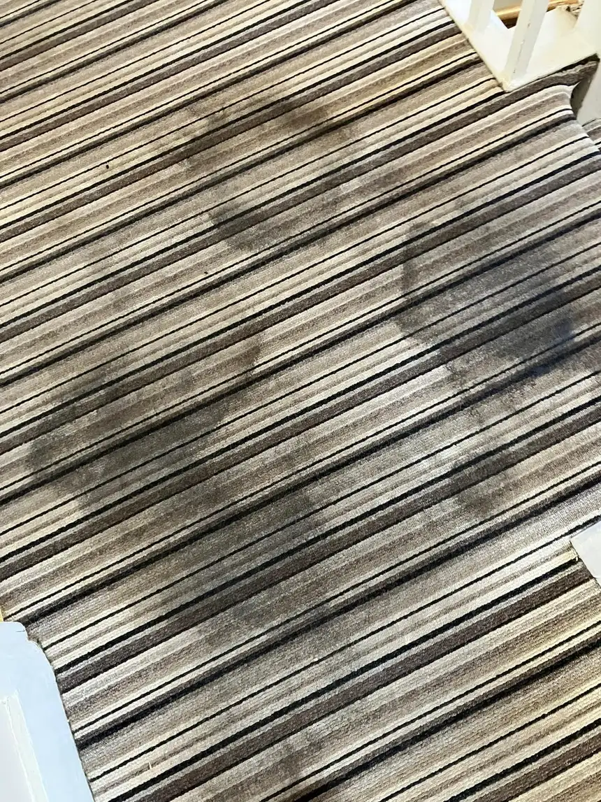 Striped brown and cream stair carpet with dark patchy marks across the treads